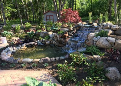 A backyard pond with waterfall and rocks, designed by a water scape contractor.